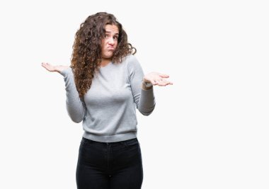 Güzel esmer kıvırcık saçlı Genç kız izole arka plan clueless ve şaşkın bir ifadeyle kollar ve eller kaldırdı üzerinde bir kazak giyiyor. Şüphe kavramı.