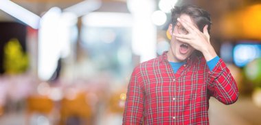 Mahcup ifadeyle parmaklarımın arasından seyir yüz ve gözler el ile kapsayan şok bakmak izole arka plan üzerinde gözlük takan genç yakışıklı adam.