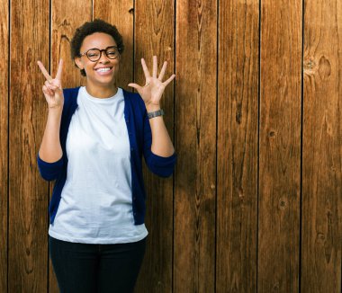 Genç güzel Afrikalı-Amerikalı kadın gözlük gösterilen ve parmakları ile işaret izole arka plan üzerinde kendinden emin ve mutlu gülümseyerek süre yedi numara.