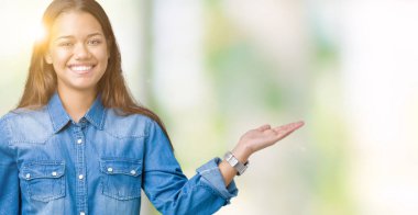 Neşeli sunulması ve kameraya bakarak avucunun ile işaret gülümseyen izole arka plan üzerinde mavi kot gömlek giyen genç güzel esmer kadın.