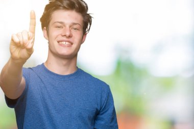 Üzerinde gösterilen ve kendinden emin ve mutlu gülümseyen bir parmak ile işaret eden oktan yukarı izole arka plan mavi t-shirt giyen genç yakışıklı adam.