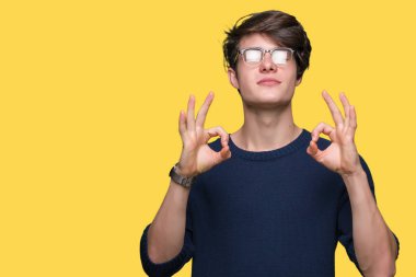Genç yakışıklı adam gözlük izole arka plan üzerinde dinlenmek ve gülümseyen gözlerle parmak ile meditasyon jest yapıyor kapalı. Yoga kavramı.