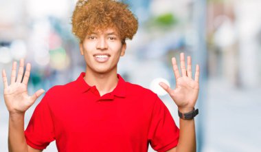 Genç yakışıklı adam ile afro saç giyen kırmızı t-shirt gösteren ve işaret yukarıya ile parmak sayı on gülümseyen güven ve mutlu.