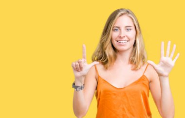 Gösterilen ve parmakları ile işaret izole arka plan üzerinde turuncu gömlek giymiş güzel genç kadın kendinden emin ve mutlu gülümseyerek süre yedi numara.