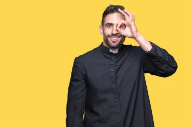 Genç Hıristiyan rahip gülümseyen, parmakları ile mutlu yüz üzerinden seyir göz el ile ok jest yapıyor izole arka plan üzerinde.