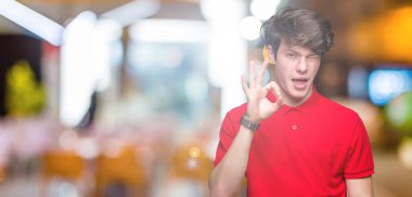 Seksi bir ifadeyle, neşeli ve mutlu yüzünü kameraya bakarak göz kırpıyor izole arka plan üzerinde kırmızı t-shirt giyen genç yakışıklı adam.