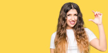 Genç güzel kadın, rahat beyaz t-shirt gülümseyen ve el ile boyut işareti yaparken parmaklar ile görünümlü ve kamera ile emin işaret giyiyor. Ölçü kavramı.