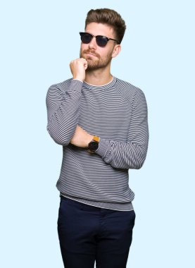 Genç yakışıklı adam çene düşünme hakkında soru, dalgın ifade üzerine el ile güneş gözlüğü takıyor. Düşünceli yüzüyle gülümsüyor. Şüphe kavramı.