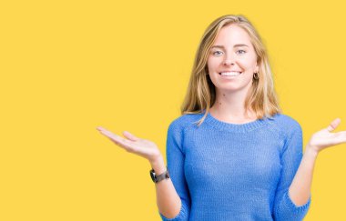 Gülen iki elle gösterilen açık avuç içi, sunma ve karşılaştırma ve denge reklam arka plan üzerinde mavi kazak giyen güzel genç kadın izole