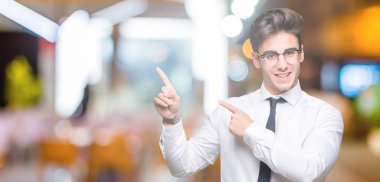 Gülümseyen ve iki elleri ve parmakları ile tarafına işaret kamera bakarak izole arka plan üzerinde gözlük takan genç iş adamı.