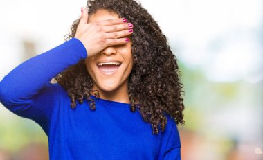 Genç güzel kadın kıvırcık saçlı kış kazak gülümsüyor ve gözleri sürpriz için kapsayan yüz el ile gülüyor. Kör kavramı.