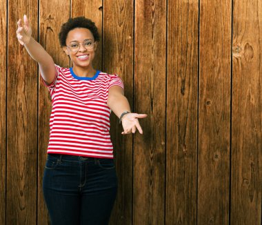 Sarılmak için kollarını açarak gülümseyerek kameraya bakarak izole arka plan üzerinde gözlük güzel genç Afro-Amerikan kadın. Neşeli ifade kucaklayan mutluluk.