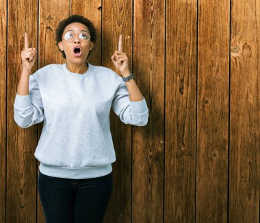 Genç güzel Afrikalı-Amerikalı kadın hayrete ve yukarıya bakıyor ve parmakları ile işaret ve silah kaldırdı sürpriz izole arka plan üzerinde gözlük.