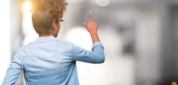 Beautiful young african american woman wearing glasses over isolated background Posing backwards pointing behind with finger hand