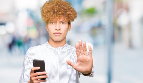 年轻的帅哥使用智能手机与张开的手做停止标志与认真和自信的表情 防御手势 — 图库照片