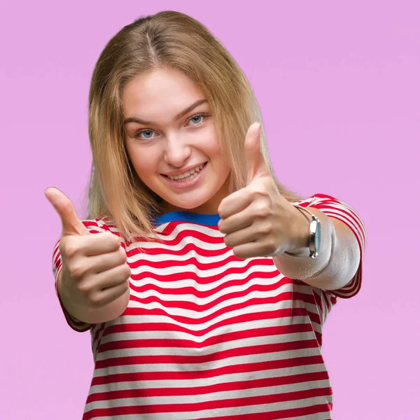 Young caucasian woman over isolated background approving doing positive gesture with hand, thumbs up smiling and happy for success. Looking at the camera, winner gesture.