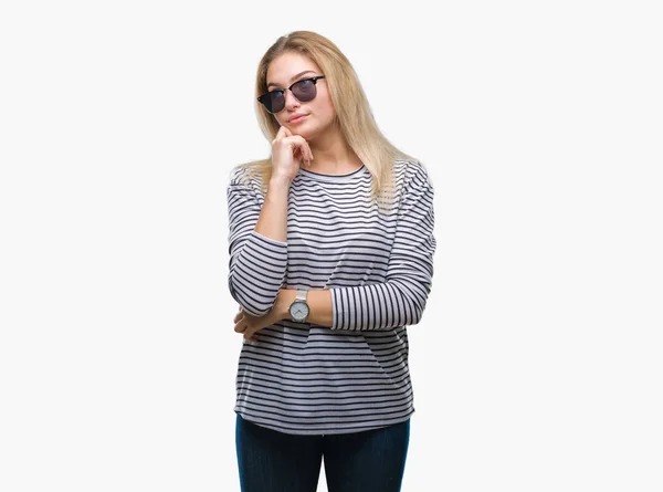 年轻的白种女人戴墨镜在孤立的背景与手在下巴思考问题 沉思的表达 微笑着体贴的脸 怀疑概念 — 图库照片