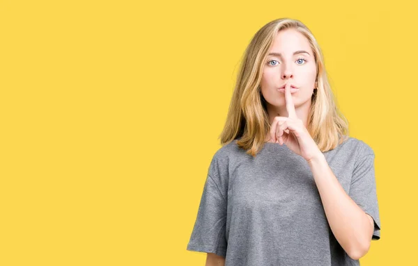 美しい若い女性の唇に指で静かにするように求めて孤立の背景に特大のカジュアルな シャツを着てします 沈黙と秘密の概念 — ストック写真