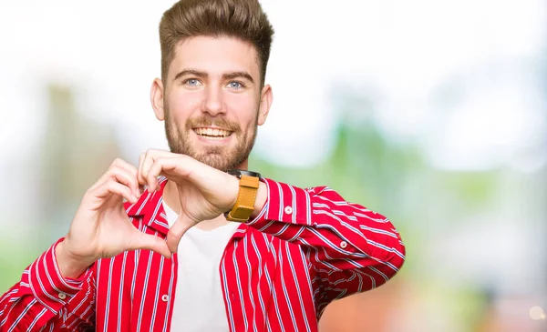 若いハンサムな男が恋ハートマークと手で形を示す笑みを浮かべて赤いシャツを着ています ロマンチックな概念 — ストック写真