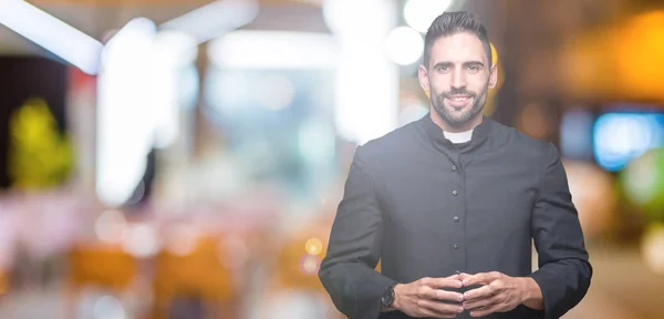 Young Christian priest over isolated background Hands together and fingers crossed smiling relaxed and cheerful. Success and optimistic