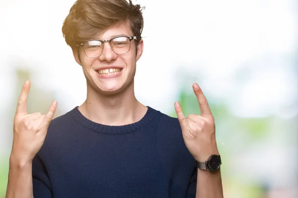 年轻的帅哥戴着眼镜在孤立的背景大喊与疯狂的表情做摇滚符号与手向上 音乐明星 沉重的概念 — 图库照片