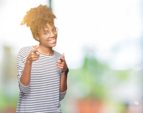 Beautiful young african american woman wearing glasses over isolated background pointing fingers to camera with happy and funny face. Good energy and vibes.