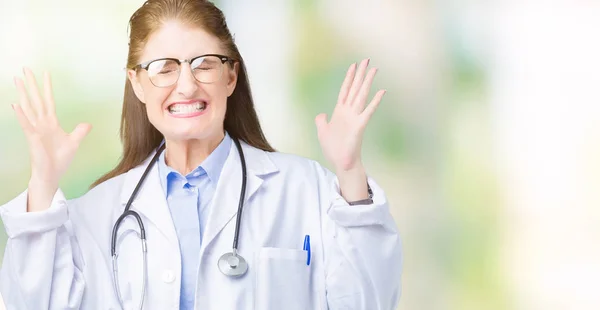 中年成熟的医生妇女穿着医疗外套在孤立的背景庆祝疯狂和疯狂的成功与手臂抬起和闭上闭上的眼睛尖叫兴奋 优胜者概念 — 图库照片