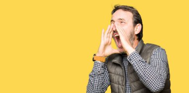 Orta yaş yakışıklı adam kızgın ile yüksek sesle bağırarak kış yelek giyen ağzına eller