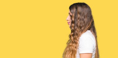 Yan bakan rahat beyaz t-shirt giyen genç güzel kadın, kendine güvenen gülümseme ile doğal yüzü ile profil poz rahat.