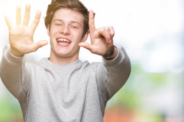 Genç yakışıklı sportif adam izole arka plan üzerinde sweatshirt giyen gösteren ve emin ve mutlu gülümserken parmakları ile yedi numara işaret.
