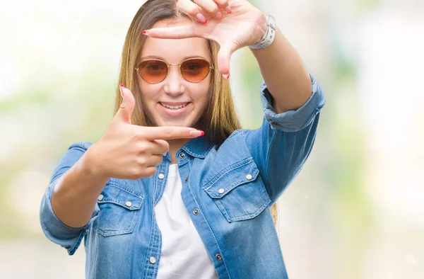Genç güzel beyaz kadın elle yapma çerçeve ve parmakları ile mutlu yüz gülümseyen izole arka plan üzerinde güneş gözlüğü takıyor. Yaratıcılık ve Fotoğrafçılık kavramı.