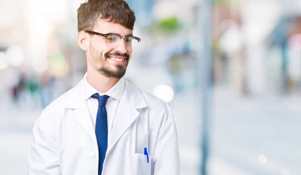 年轻的专业科学家男子穿着白色外套在孤立的背景看着一边面带微笑 自然的表情 笑自信 — 图库照片