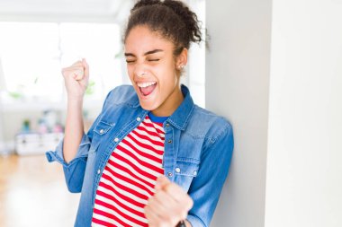 Afro saç ile güzel genç Afrikalı Amerikan kadın rahat denim ceket giyen silah ile başarı için heyecanlı gülümseyen zafer kutluyor kaldırdı. Kazanan kavramı.