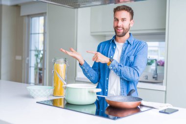Yakışıklı adam mutfakta İtalyan spagetti makarna pişirme şaşırttı ve el ile sunarken kameraya gülümseyerek ve parmak ile işaret.