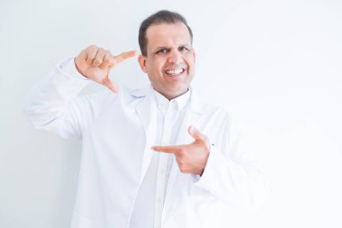 Orta yaş doktor adam beyaz arka plan üzerinde tıbbi ceket giyen mutlu yüz ile elleri ve parmakları ile çerçeve yapma gülümseyerek. Yaratıcılık ve fotoğrafçılık konsepti.