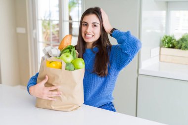 Baş, el ile vurguladı sağlıklı yiyecek dolu kese kağıdı tutan güzel genç kadın şok utanç ve sürpriz suratla, öfkeli ve sinirli. Korku ve hata için üzgün.