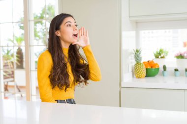 Evde beyaz masada genç güzel kadın bağırıyor ve ağzıyla yan yana yüksek sesle bağırıyor. İletişim kavramı.