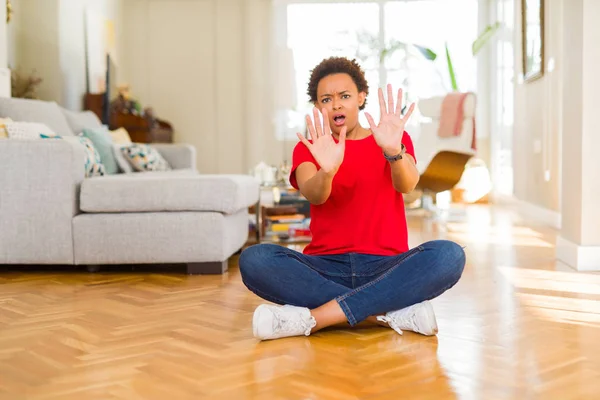 若い美しいアフリカ系アメリカ人の女性が自宅で床の上に座って恐怖表現を恐れて手でジェスチャーを停止し ショックで叫んで恐れている パニック概念 — ストック写真