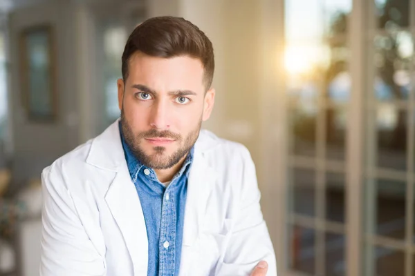 Young handsome doctor man at the clinic skeptic and nervous, disapproving expression on face with crossed arms. Negative person.