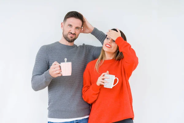 Young couple drinking cup of coffee over isolated background stressed with hand on head, shocked with shame and surprise face, angry and frustrated. Fear and upset for mistake.