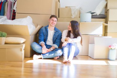 Evde karton kutular etrafında yerde oturan rahatlatıcı genç güzel çift, yeni bir eve hareket mutlu gülümseyen