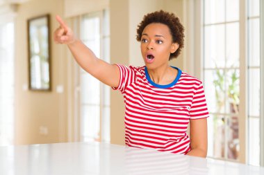 Genç ve güzel afro-amerikan kadın evde parmağıyla işaret ederek ileriyi işaret ediyor, ağzı açık hayret verici bir ifade, önünde bir şey.