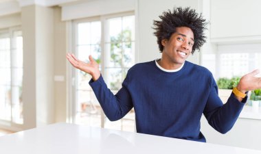 Rahat bir süveter giyen genç Afro-Amerikan adam evde oturmuş gülümsüyor iki elini de açık tutuyor, sunuyor ve reklam karşılaştırması yapıyor ve dengeyi sağlıyor.