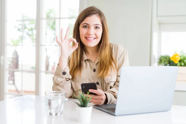 指でOkサインをやってスマートフォンやコンピュータを使用して美しい若い女性 優れたシンボル — ストック写真