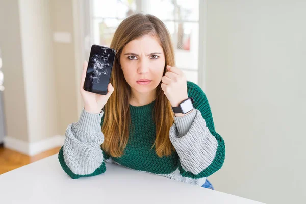 Beautiful young woman holding broken smartphone annoyed and frustrated shouting with anger, crazy and yelling with raised hand, anger concept