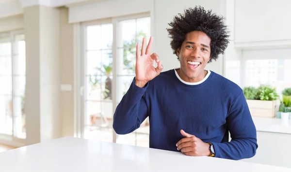 若いアフリカ系アメリカ人の男性のカジュアルなセーターを自宅で笑顔積極的な手と指でOkのサインをやって座っている 成功した表現 — ストック写真