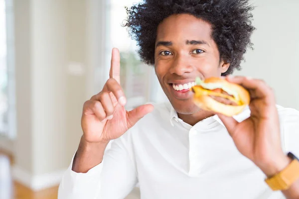 昼食にハンバーガーを食べるアフリカ系アメリカ人の空腹の男は 幸せな顔で指を指すアイデアや質問に驚いた ナンバーワン — ストック写真