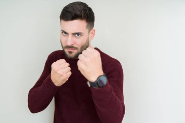 Soyutlanmış arka planda süveter giyen genç yakışıklı adam yumruk savunma hareketleriyle dövüşmeye hazır kızgın ve üzgün bir yüz, sorundan korkuyor.