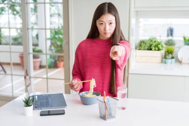 Güzel Asyalı kadın dizüstü bilgisayar kullanarak çalışan ve kamera ve size parmak ile işaret asya erişte yeme, el işareti, önden olumlu ve kendinden emin jest