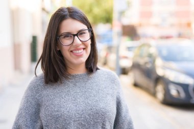 Genç güzel kadın gözlük giyerek şehir kasabasında sokakta emin yürüyüş gülümsüyor